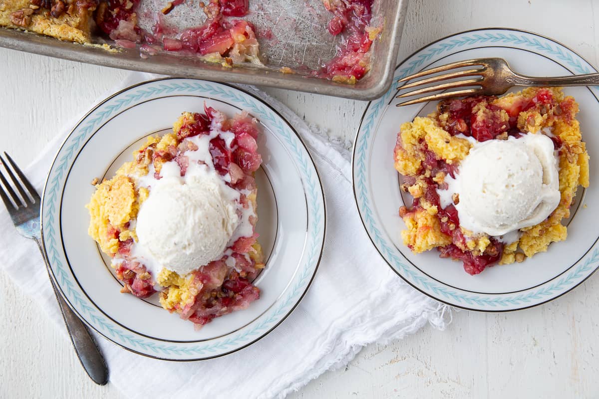 blue rimmed white plates with cherry dump cake, topped with ice cream.