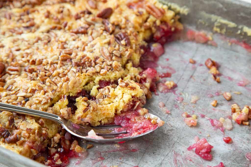 cherry dump cake in a metal pan with a metal spoon.