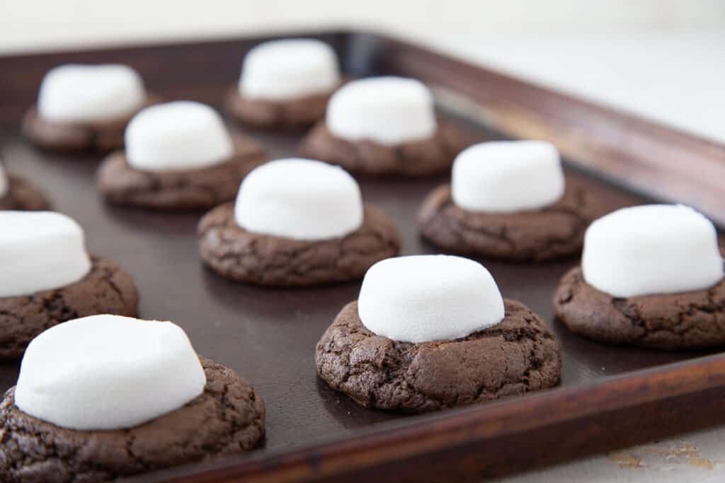 chocolate cookies topped with half a marshmallow on each on a sheet pan.