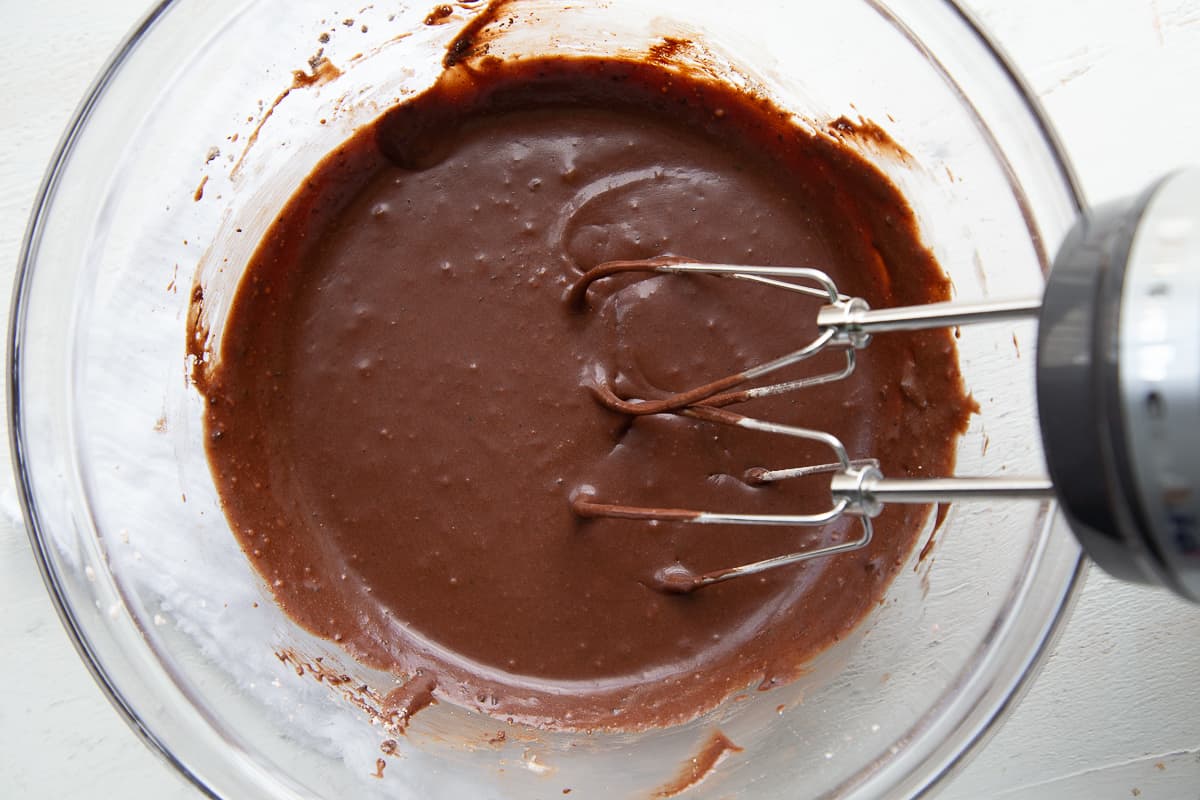 fudge icing in a glass bowl with a hand mixer also in the bowl.