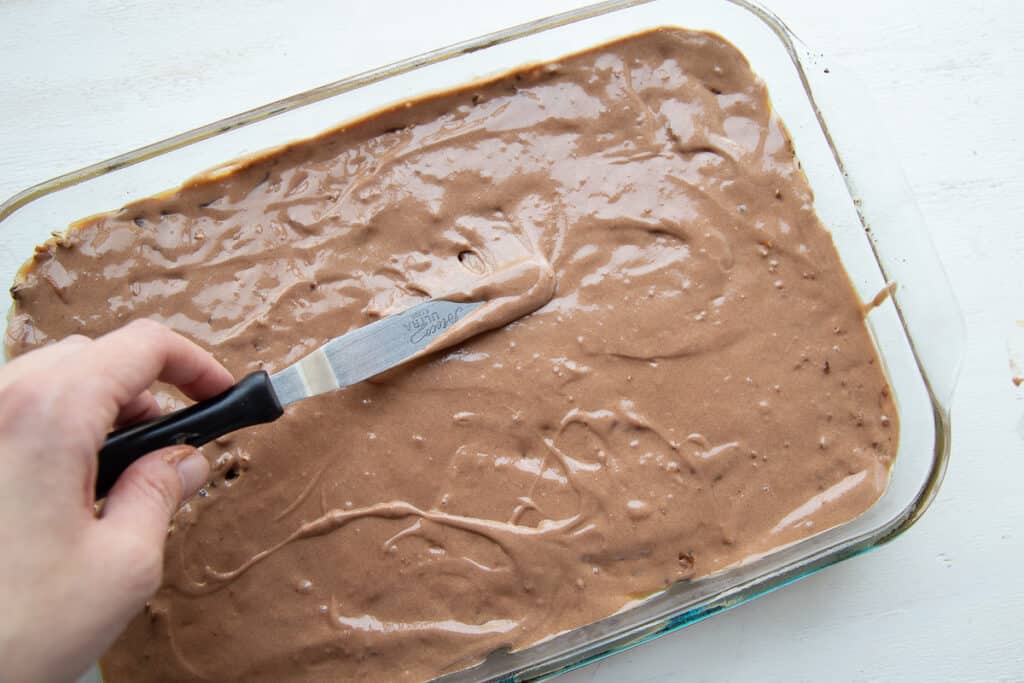offset spatula spreading cake batter in a glass 13x9 inch pan.
