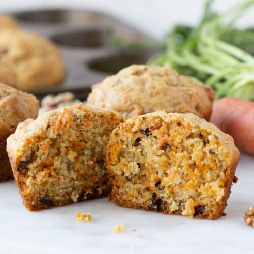 carrot muffin cut in half, with whole muffins and whole carrots in the background.