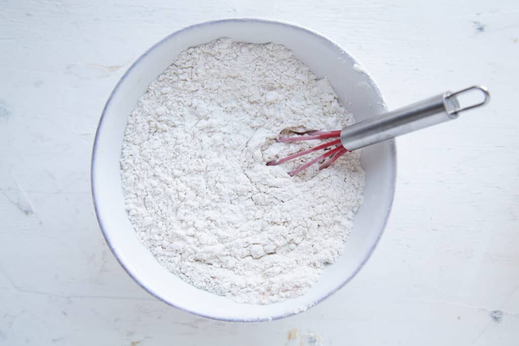dry ingredients for carrot muffins in a white bowl with a red whisk.