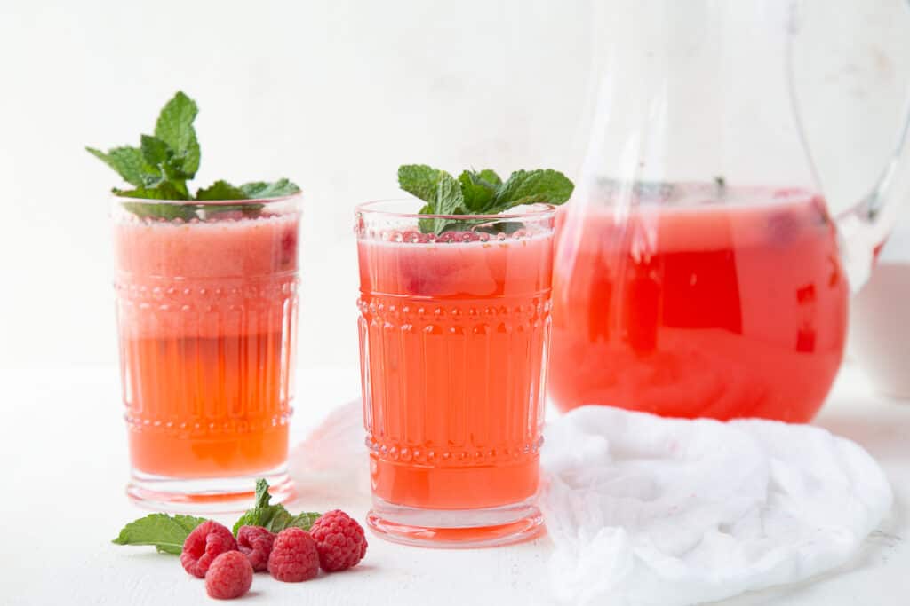 glasses of raspberry lemonade next to a pitcher and fresh raspberries.