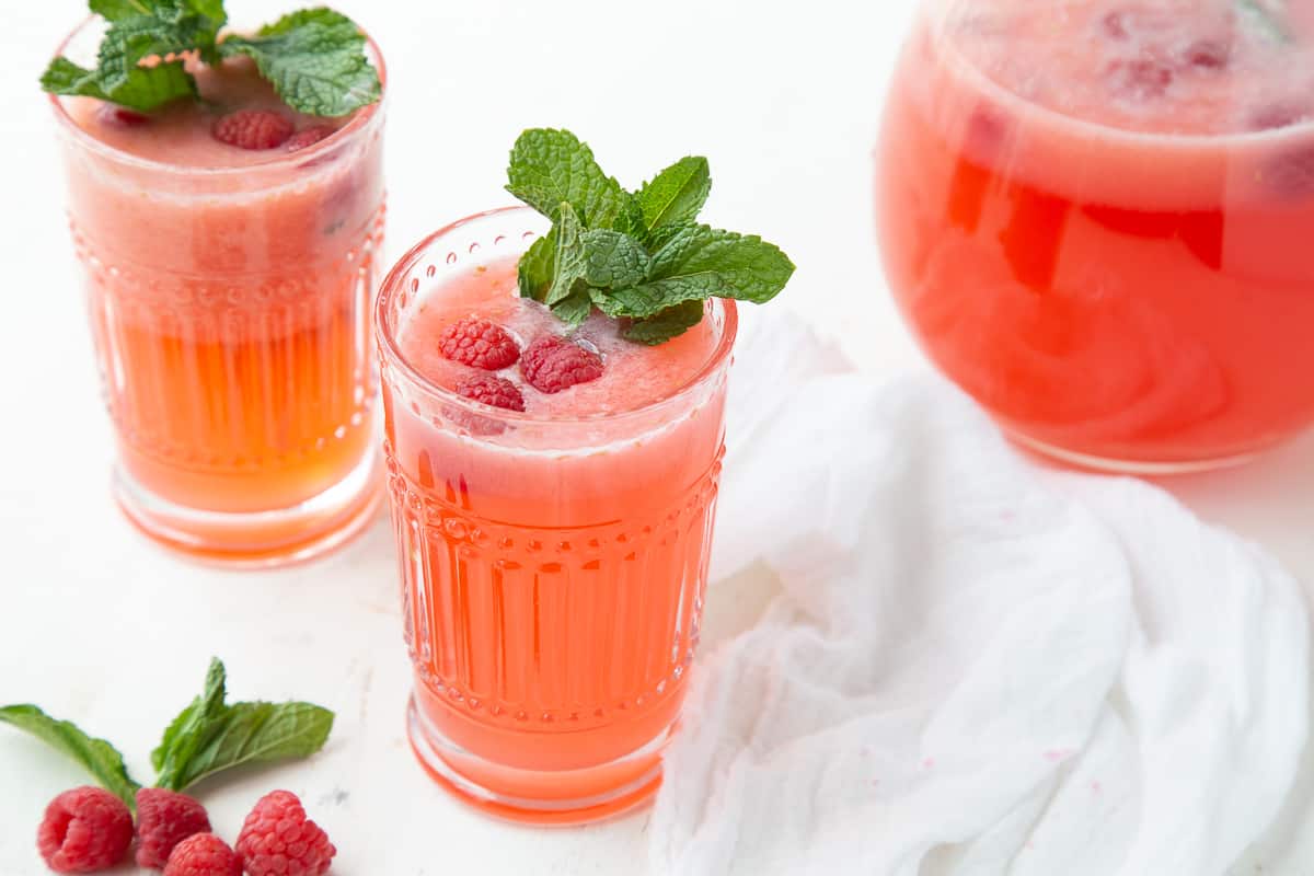 glasses of raspberry lemonade next to a glass pitcher.