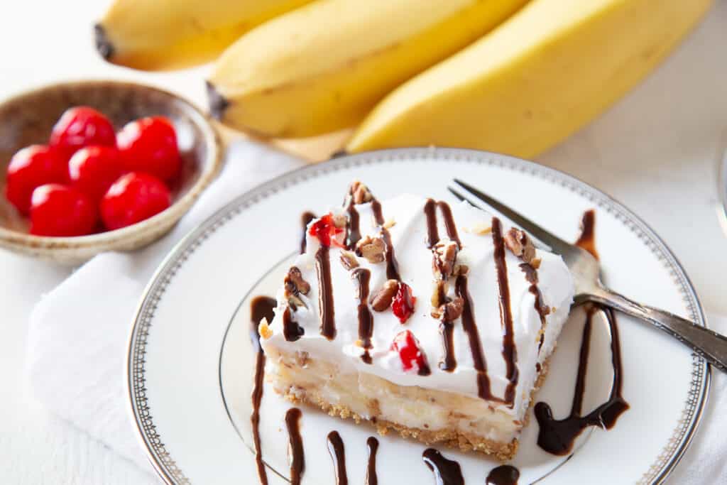slice of banana split cake topped with chocolate sauce on a white plate.