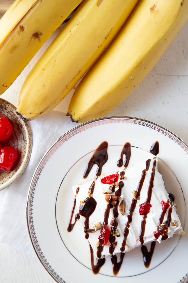 banana split cake slice with chocolate drizzle on a white plate.