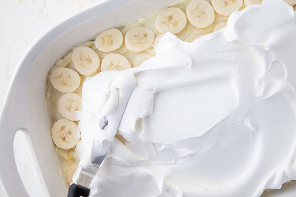 offset spatula spreading whipped cream over banana slices.