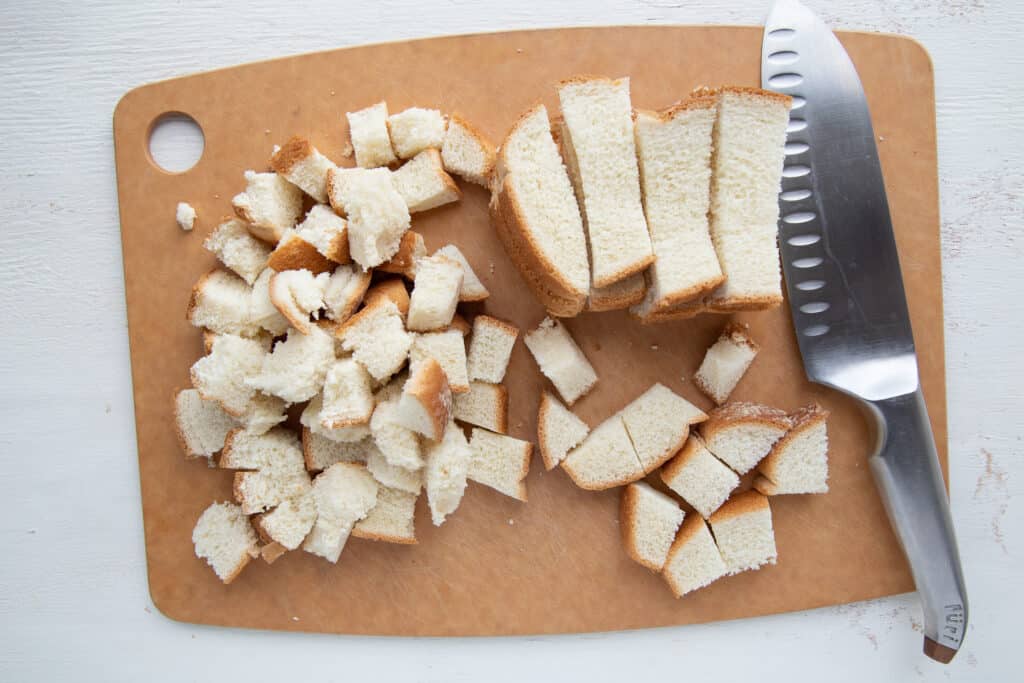 cubes of bread and a knife on a wooden cutting board.