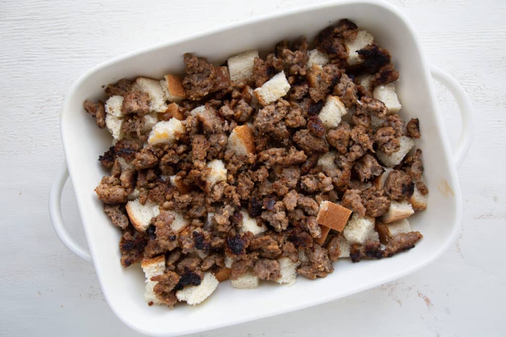 cubed bread and crumbled sausage in a white casserole dish.
