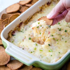 hand scooping up reuben dip with a rye chip from a casserole dish.