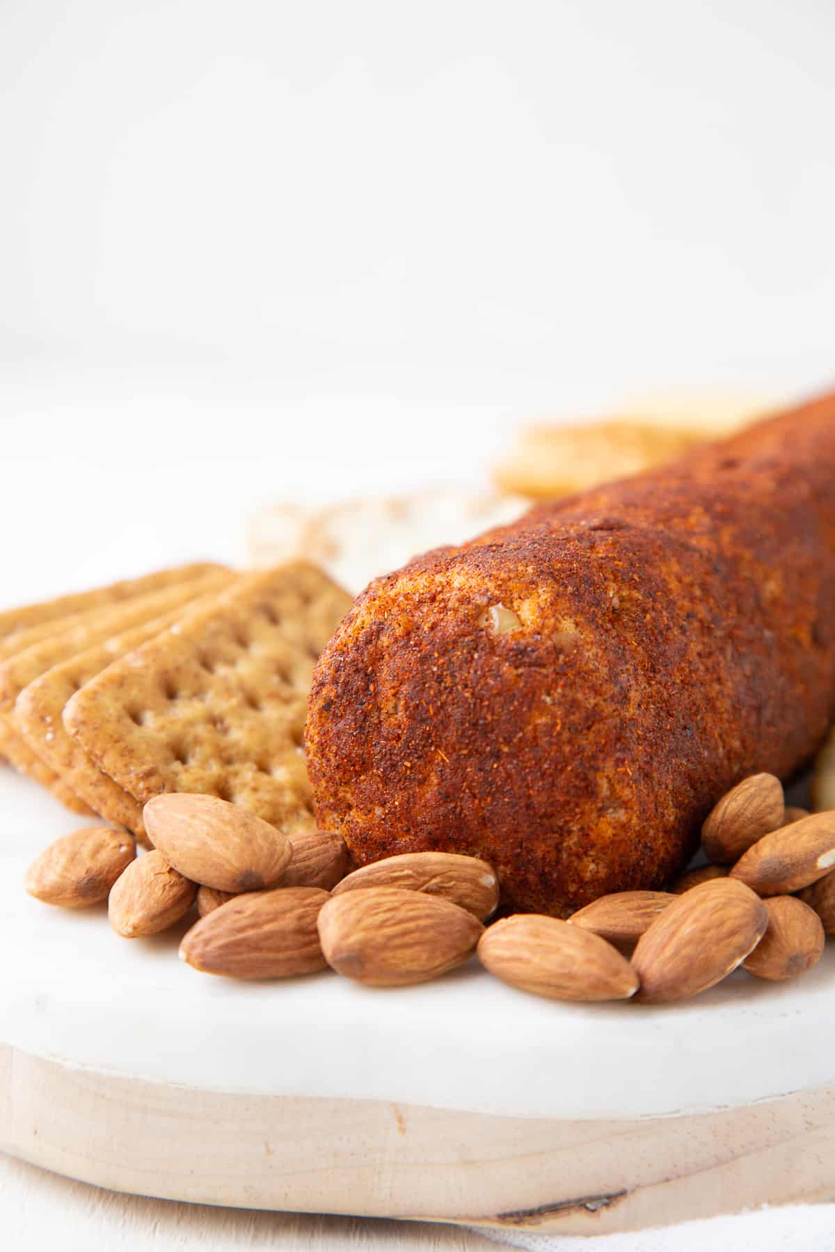 cheese log next to crackers and almonds on a white platter.