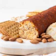 cheese roll on a marble board with crackers and almonds.