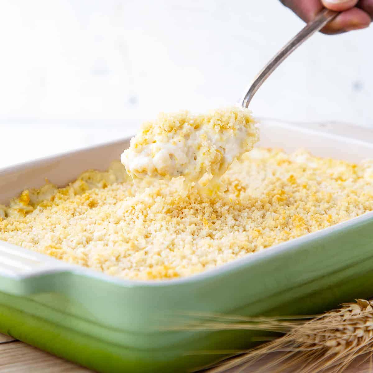 hand lifting a spoon of cheesy corn casserole out of a casserole dish.