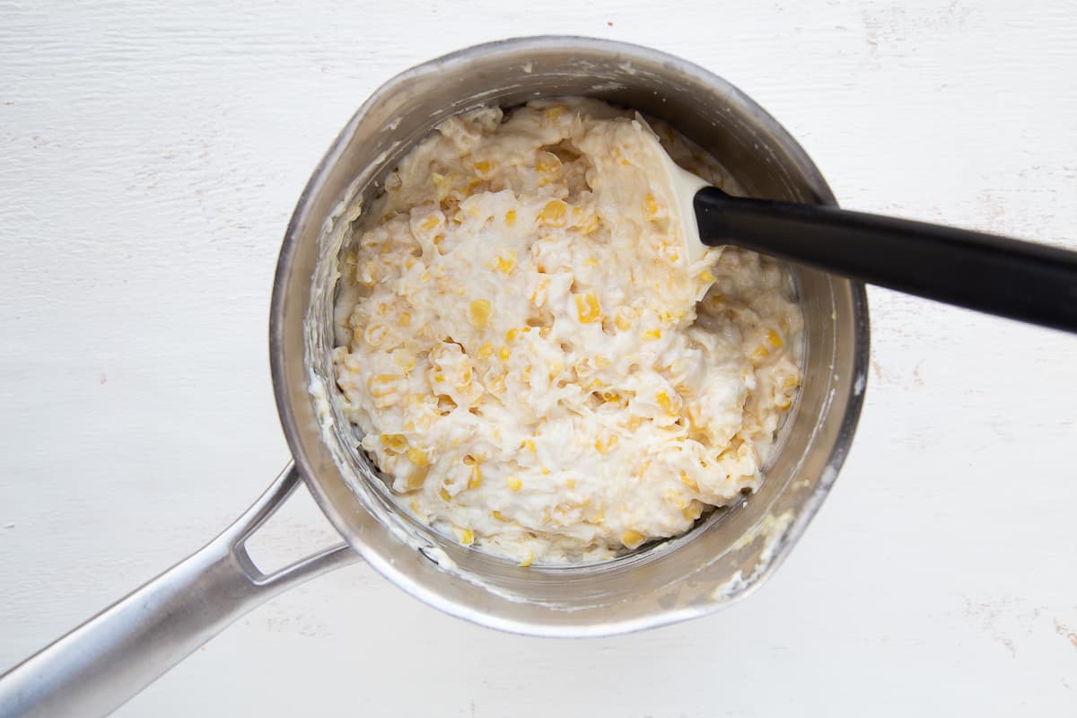 corn and cheese in a saucepan with a spatula.