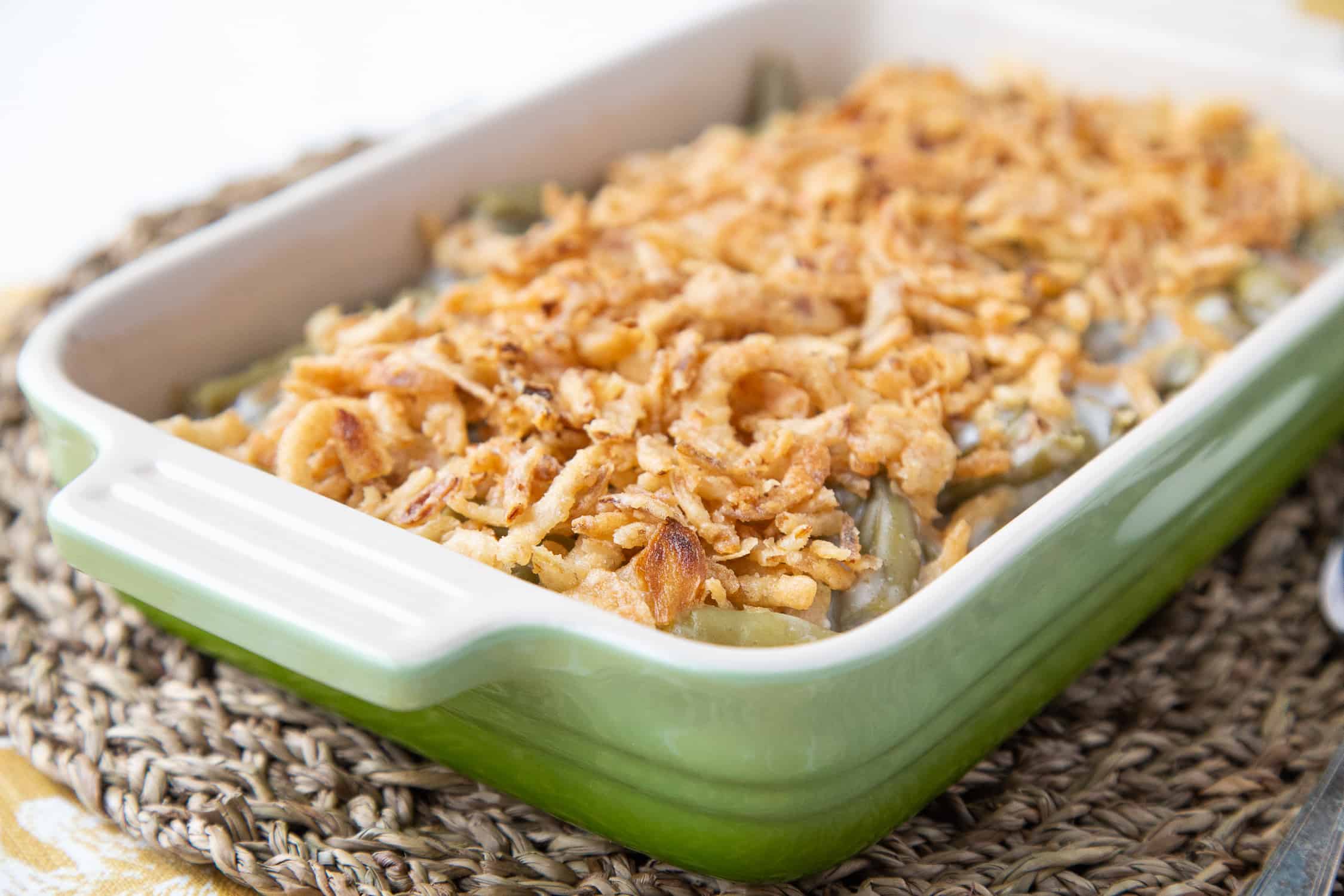 green bean casserole in a green casserole dish on a woven placemat.