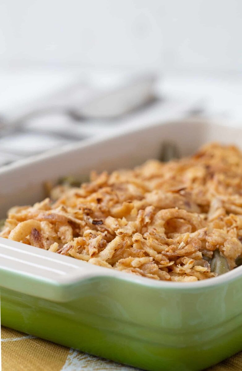 green casserole dish filled with green bean casserole with serving utensils in the background.