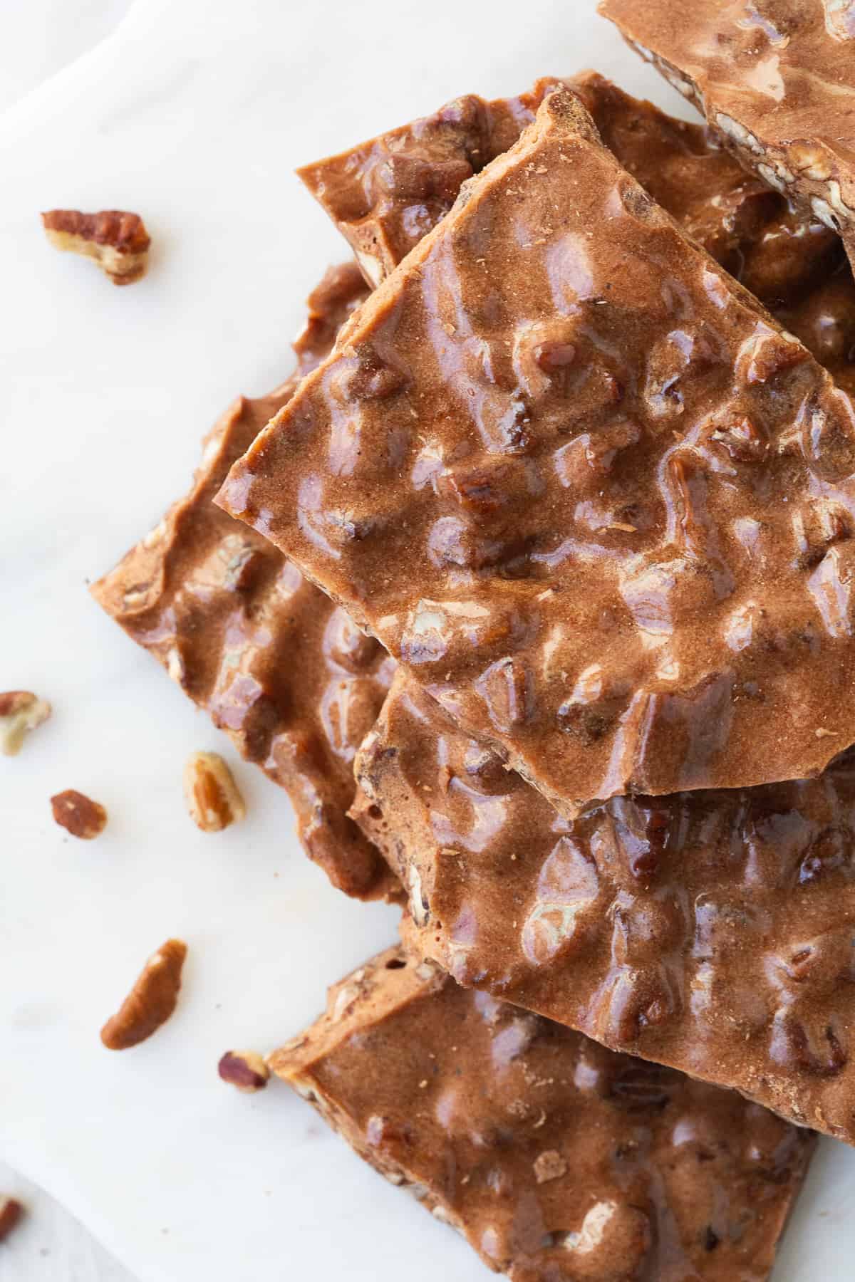 peanut brittle with loose pecans on a white marble platter.