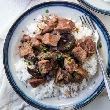 beef stew over rice on a blue rimmed plate.