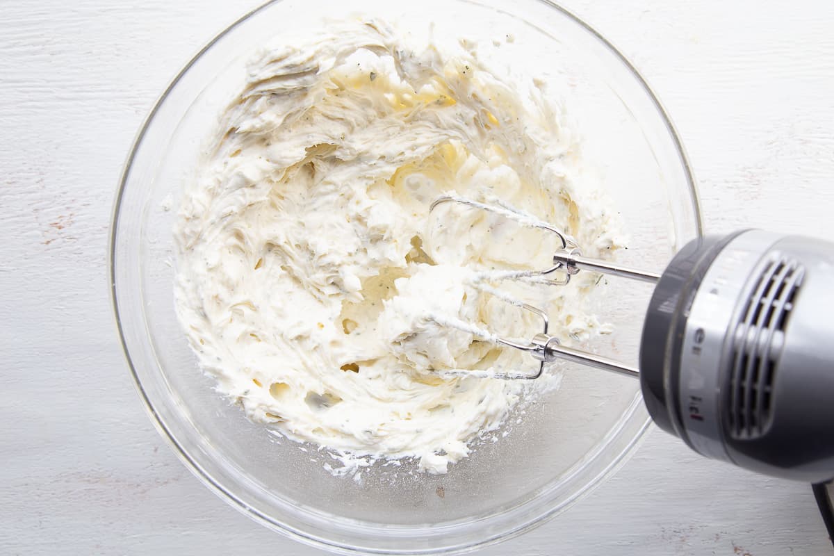 cream cheese spread in a glass bowl with a hand mixer.