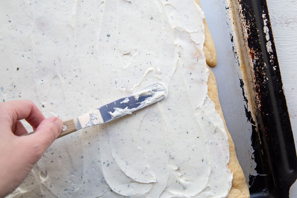 hand spreading cream cheese onto dough with an offset spatula.