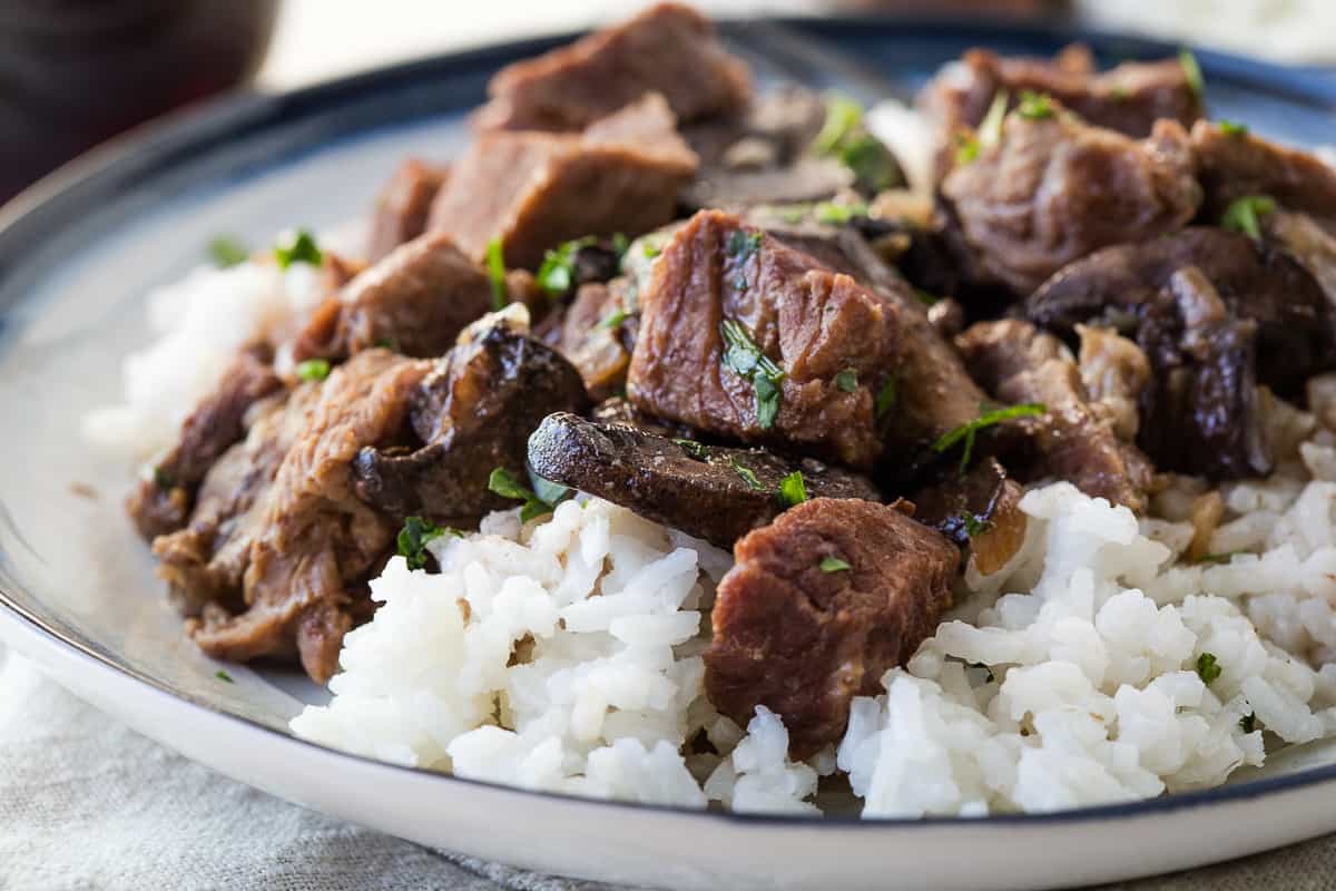 beef stew with mushrooms over rice on a blue and white plate.