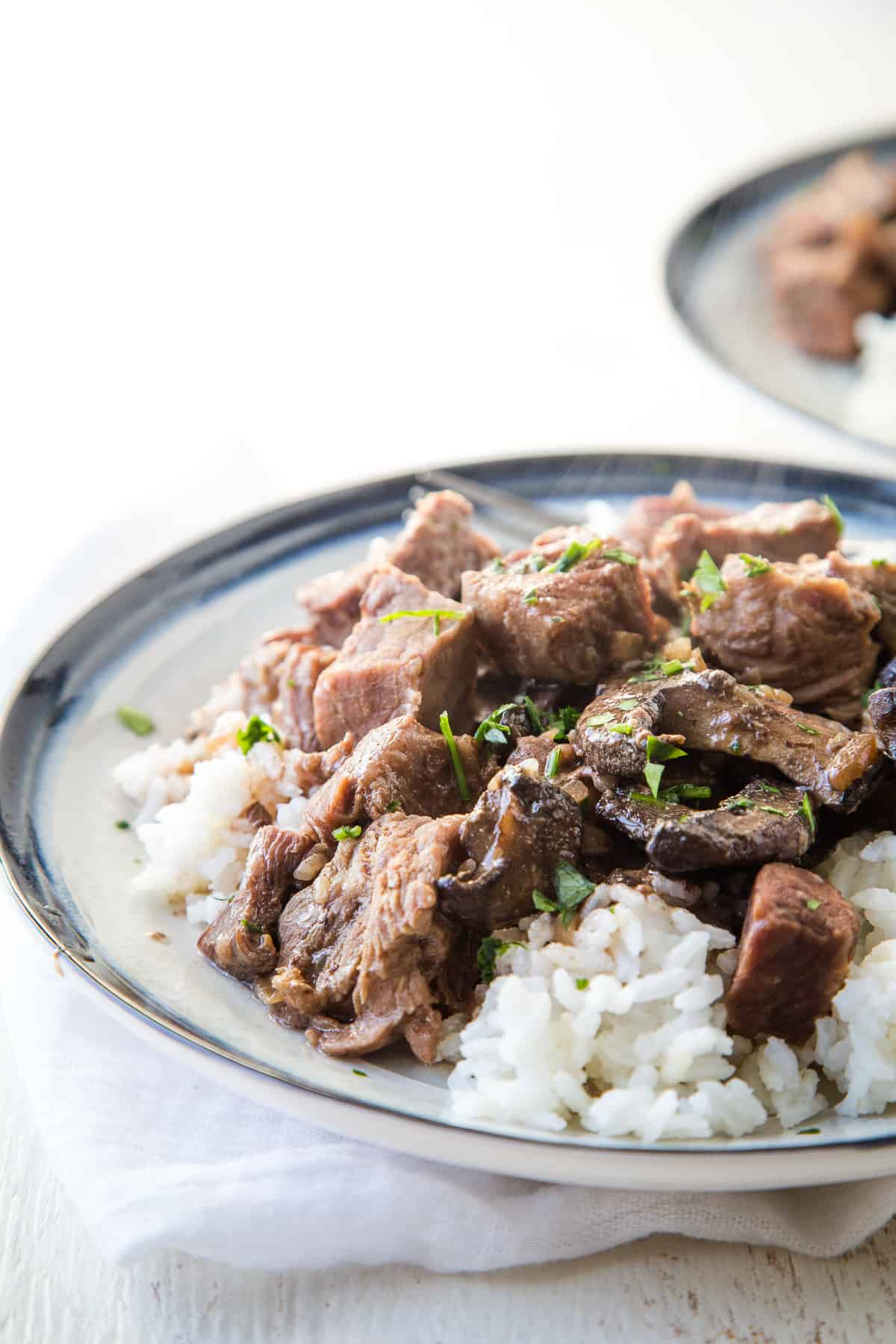 crockpot beef stew over rice on a blue rimmed plate.