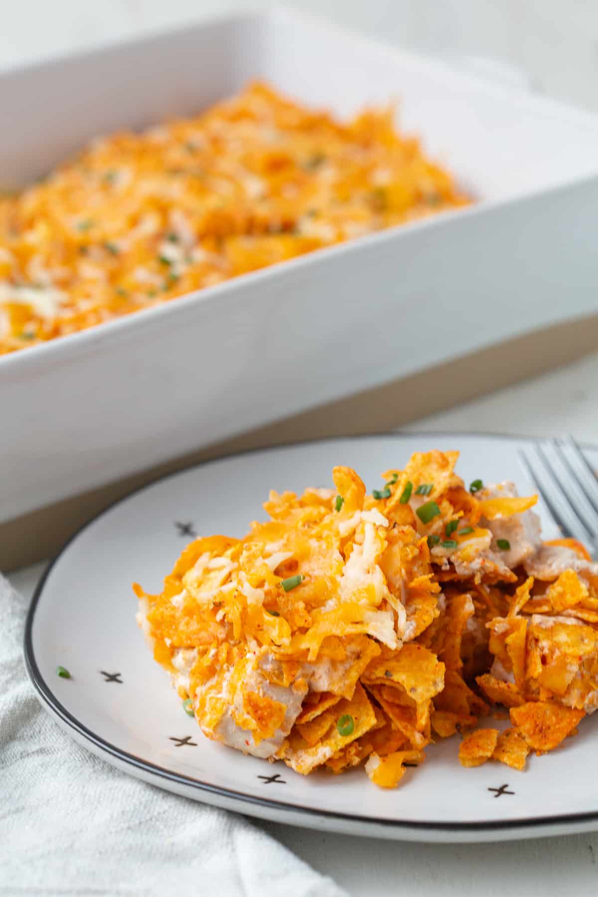 chicken dorito casserole on a white plate next to a whole casserole dish.