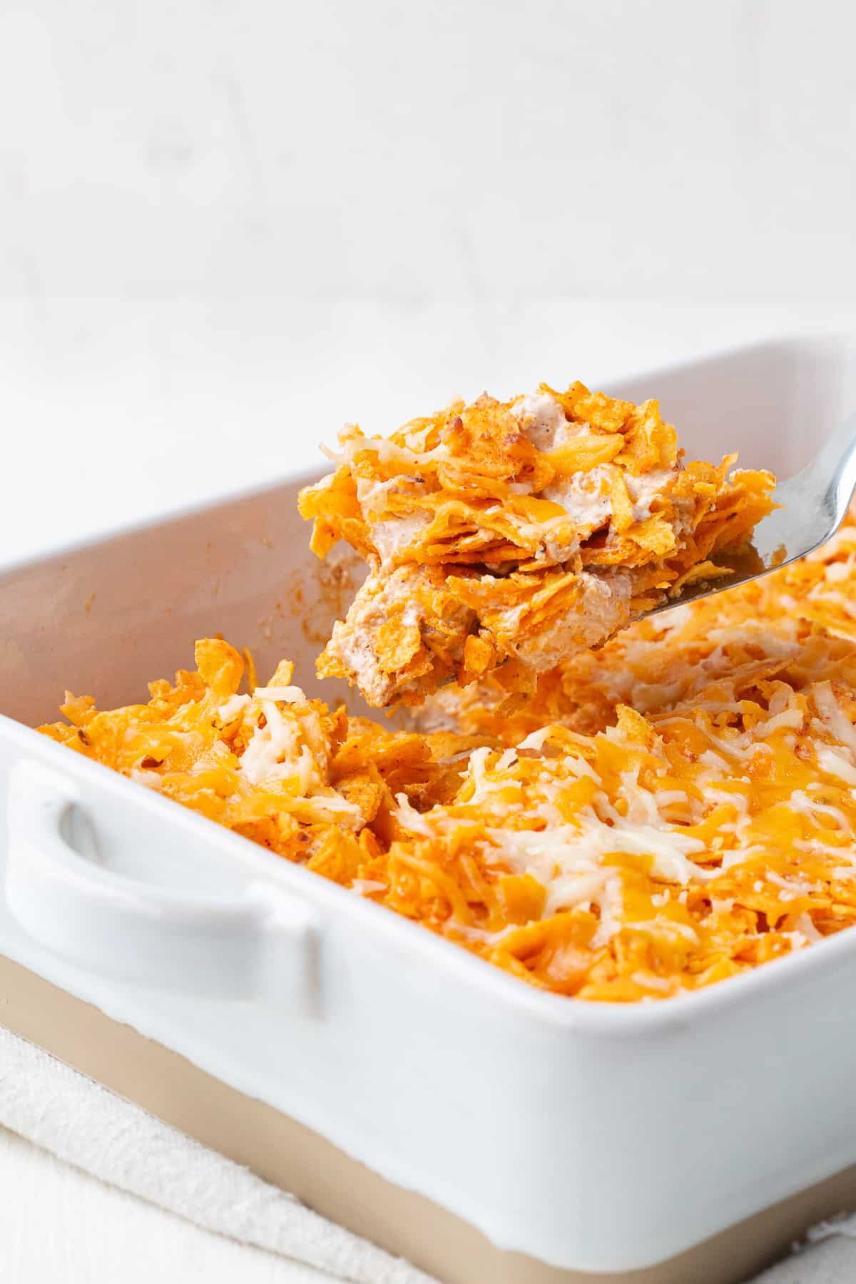 metal spatula lifting up a serving of dorito chicken casserole from a white casserole dish.
