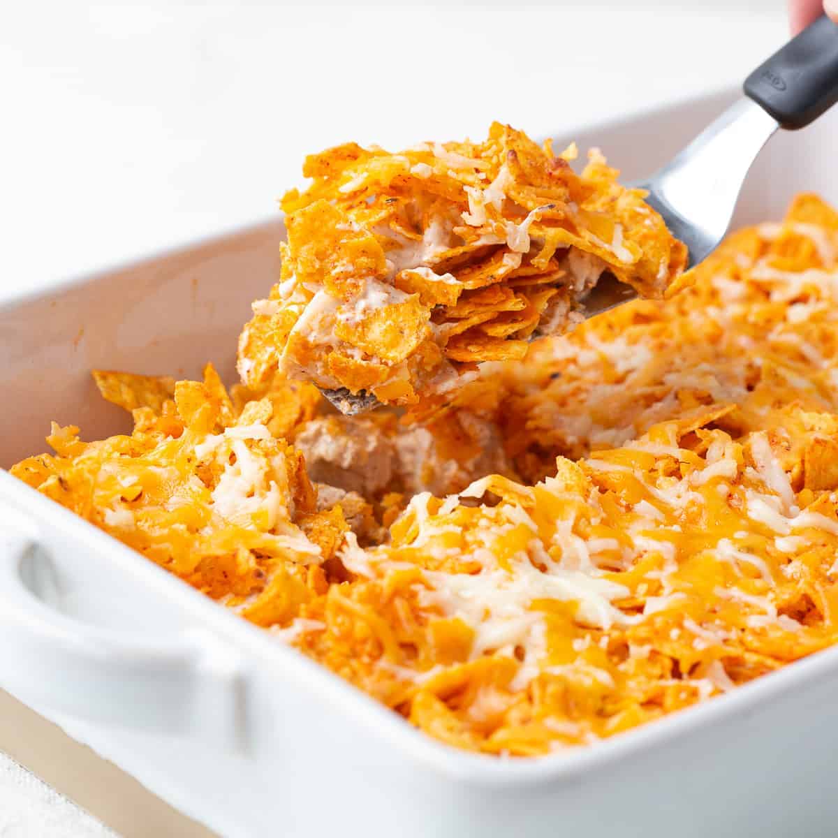 hand scooping up dorito chicken casserole with a spatula.