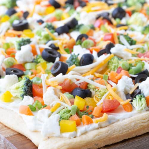 crescent roll veggie pizza on a wooden cutting board.