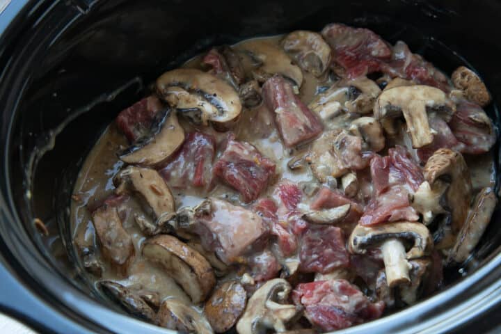 uncooked beef stew and mushrooms in a crockpot.