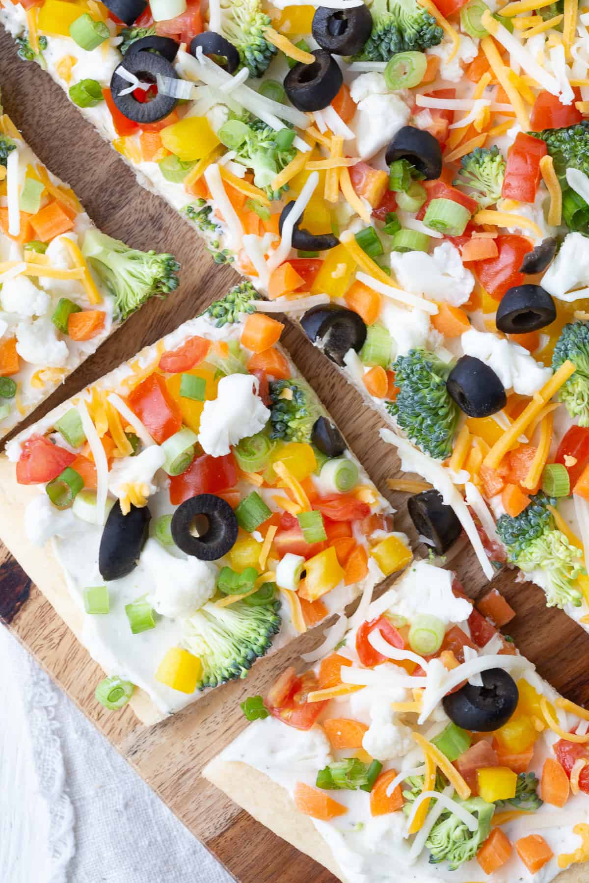 slices of crescent roll veggie pizza on a wooden cutting board.