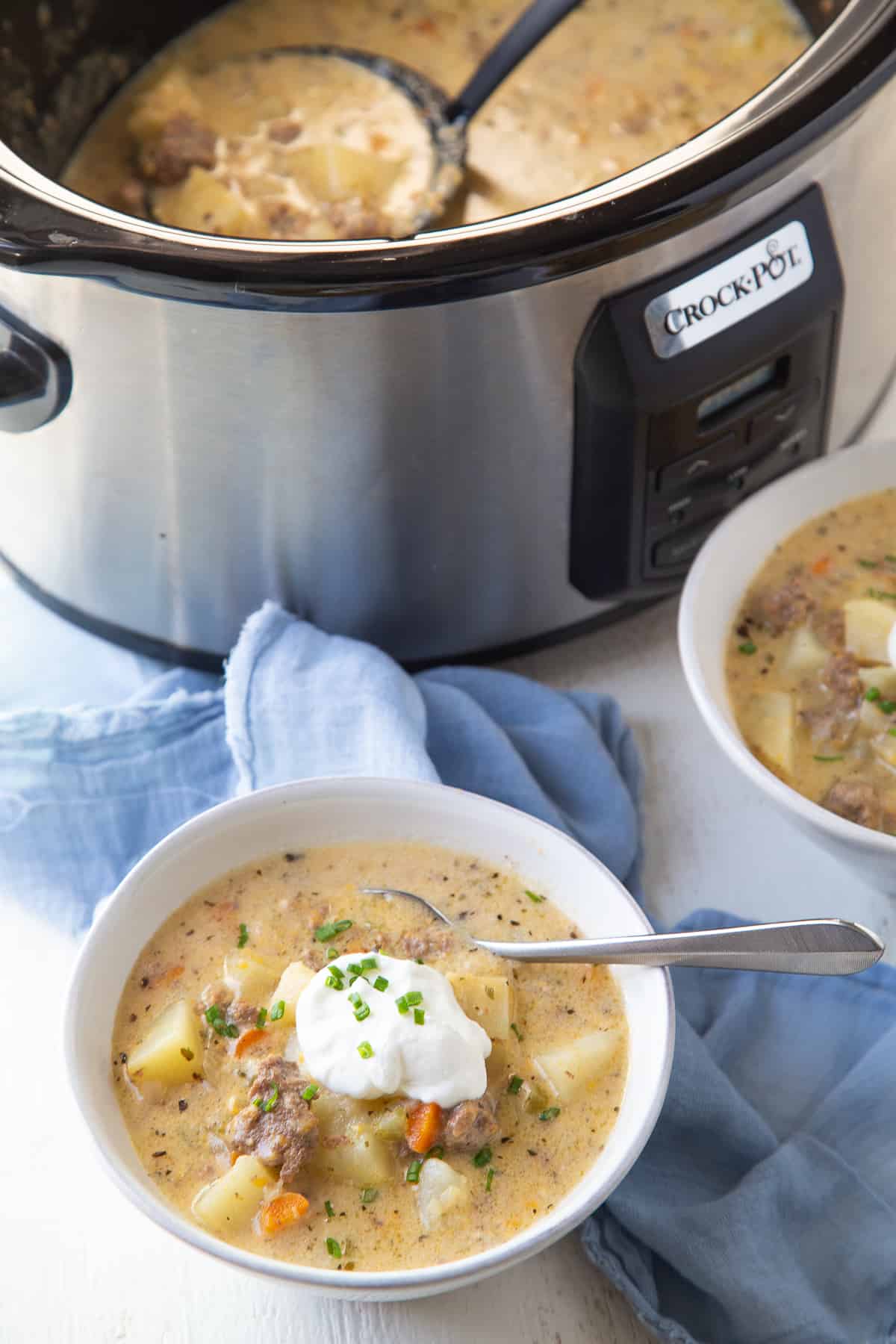 bowl of cheeseburger soup next to a crockpot full of more soup.