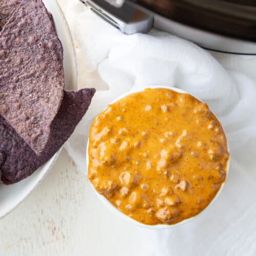 white ramekin of chili cheese dip next to a bowl of blue corn tortilla chips.