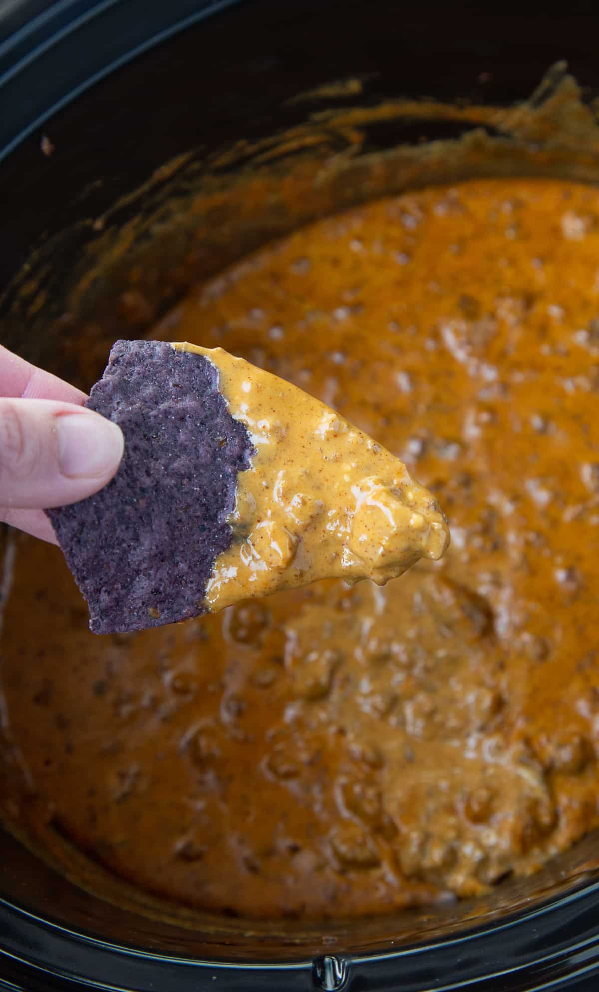 hand dipping a chip into chili cheese dip.