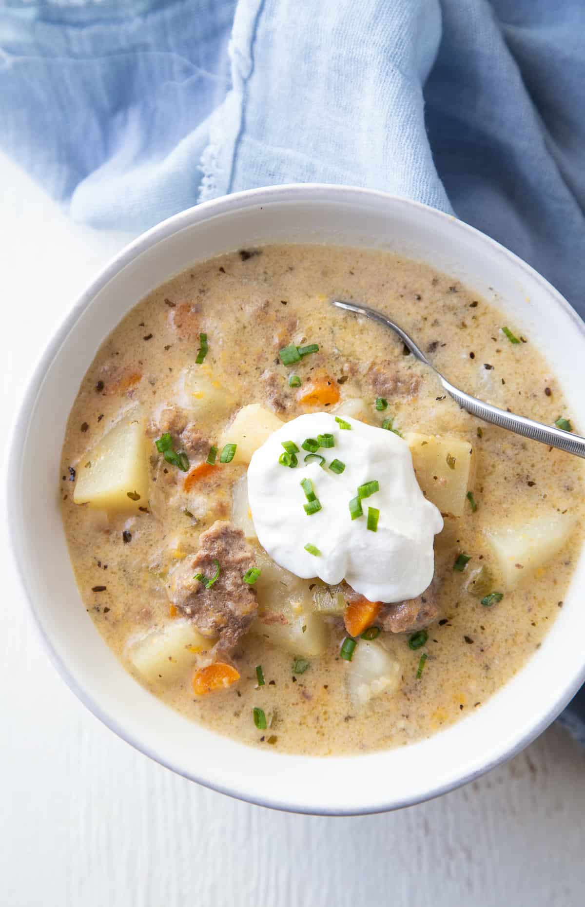 white bowl of crockpot cheeseburger soup with a blue napkin.