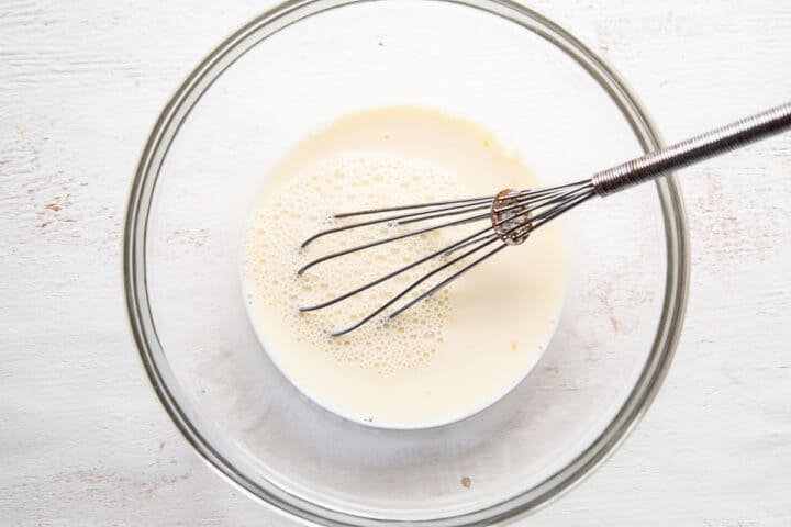 milk and egg mixture with a whisk in a glass bowl.