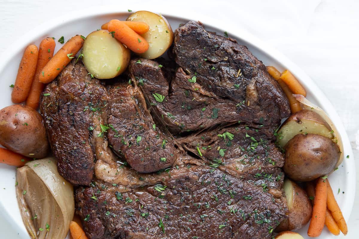 chuck roast on a white platter with carrots and potatoes.