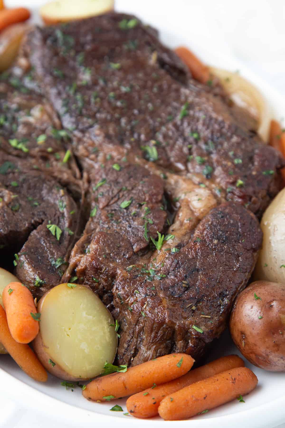 chuck roast on a white platter with carrots and potatoes.