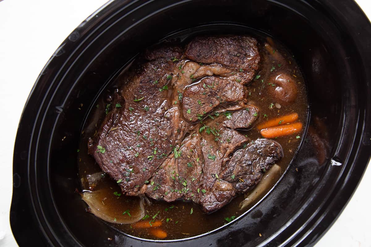 cooked pot roast with carrots in a crockpot.