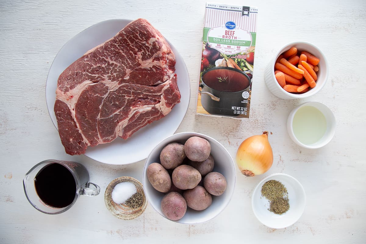 chuck roast, potatoes, carrots, and other ingredients on a white table.