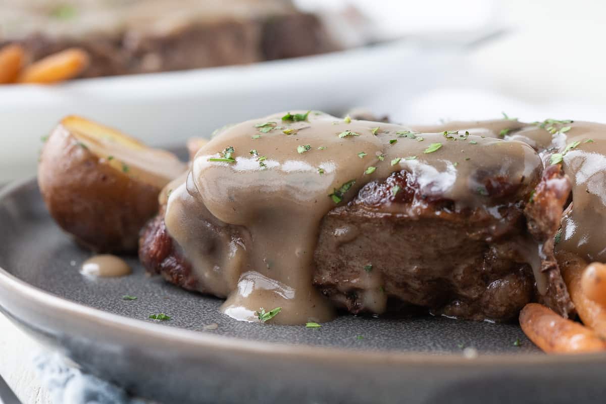 slice of pot roast topped with thick gravy on a gray plate.