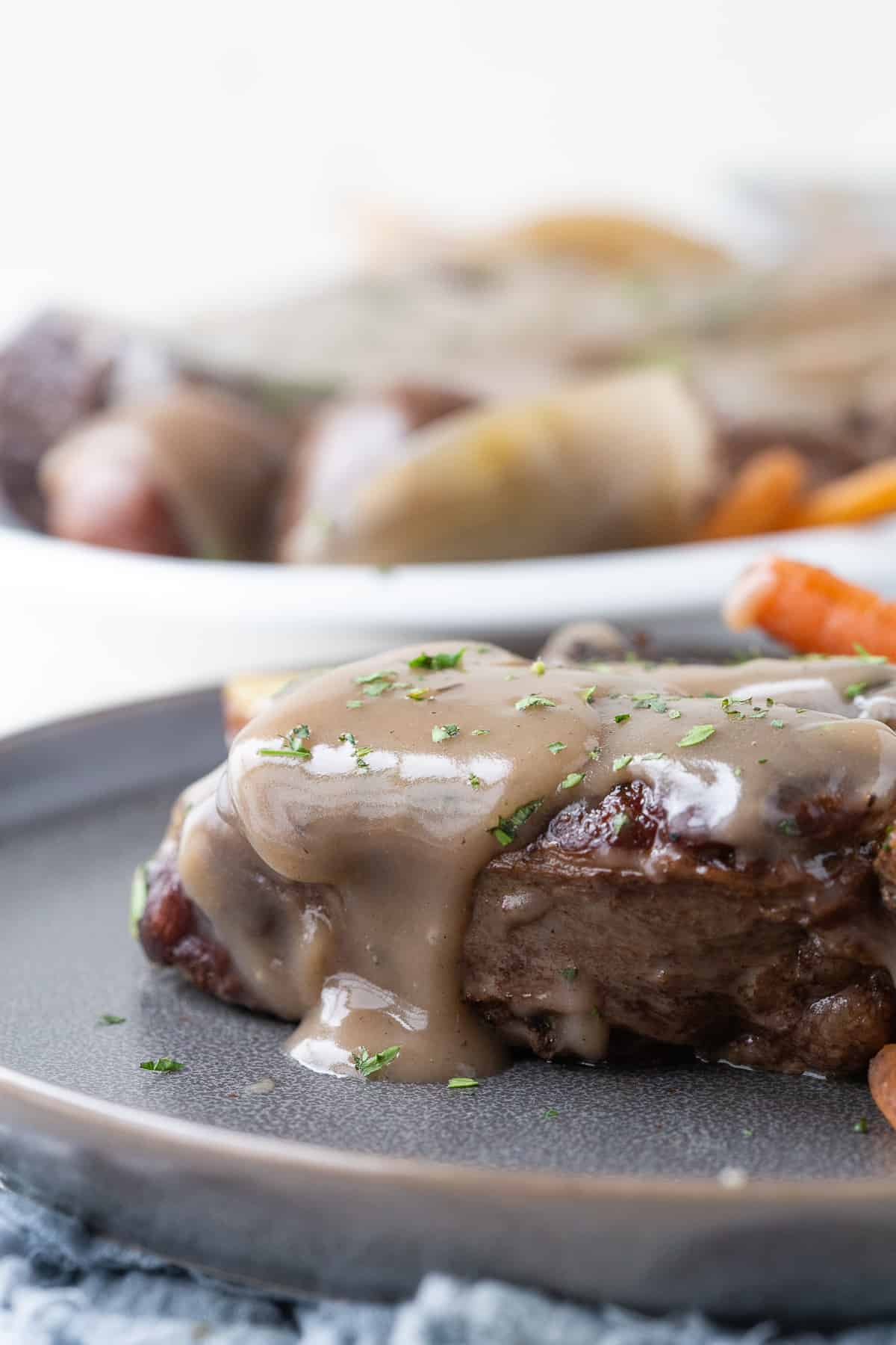 piece of pot roast topped with brown gravy on a gray plate.