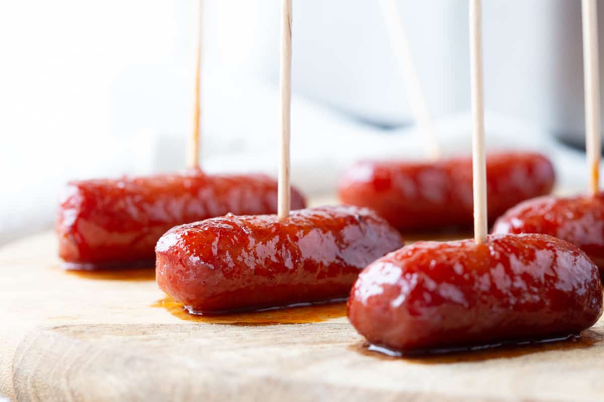 little smokies with grape jelly and chili sauce on toothpicks on a wooden board.