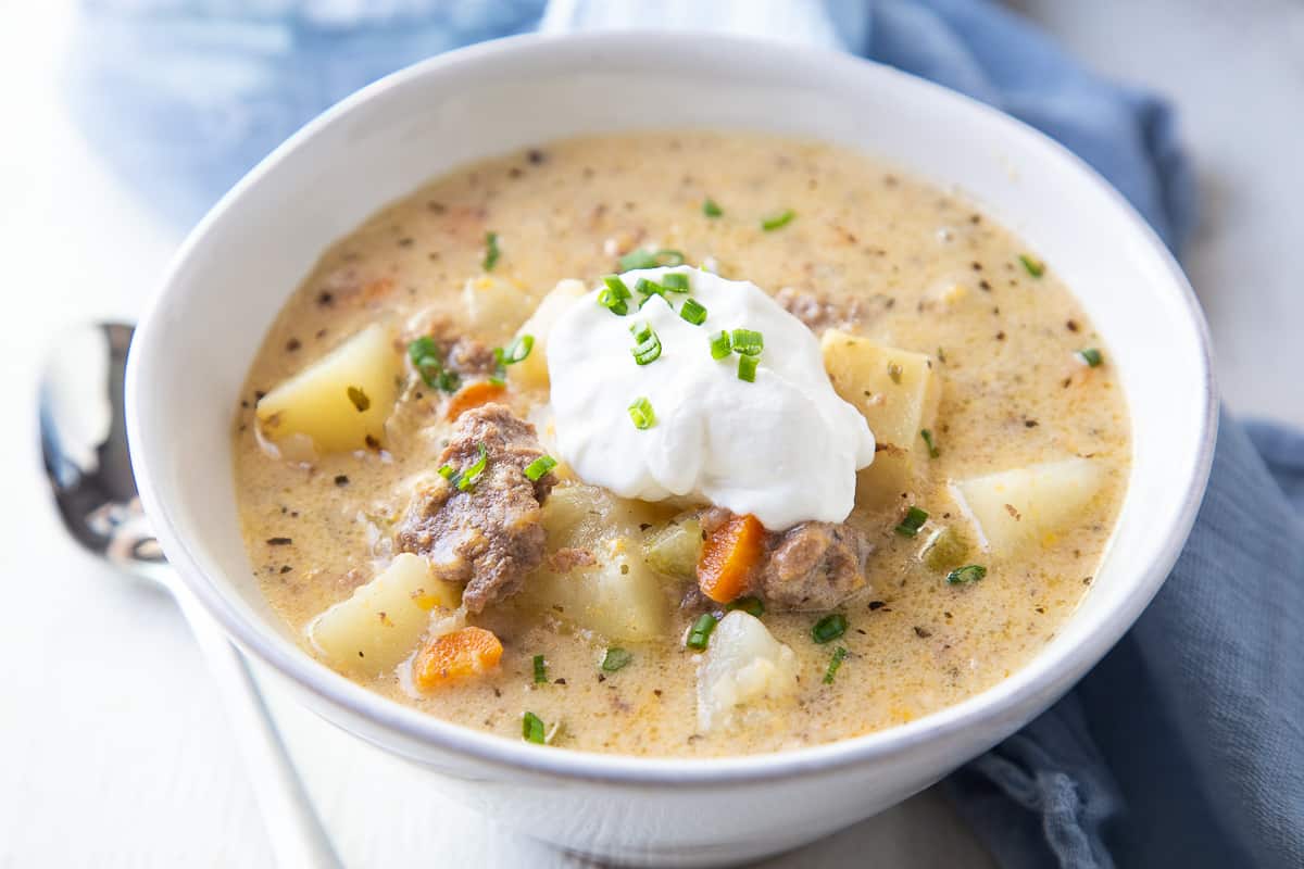 bowl of cheeseburger soup with sour cream and chives next to a spoon.