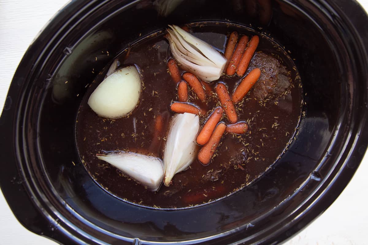 carrots, onions, and an uncooked roast in a crockpot.