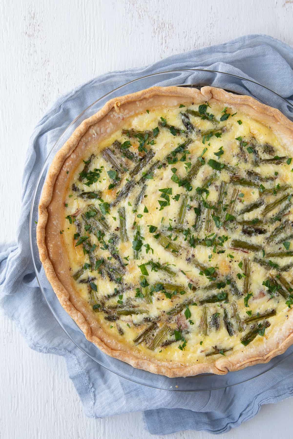 asparagus, ham, and gruyere quiche on a blue tea towel.