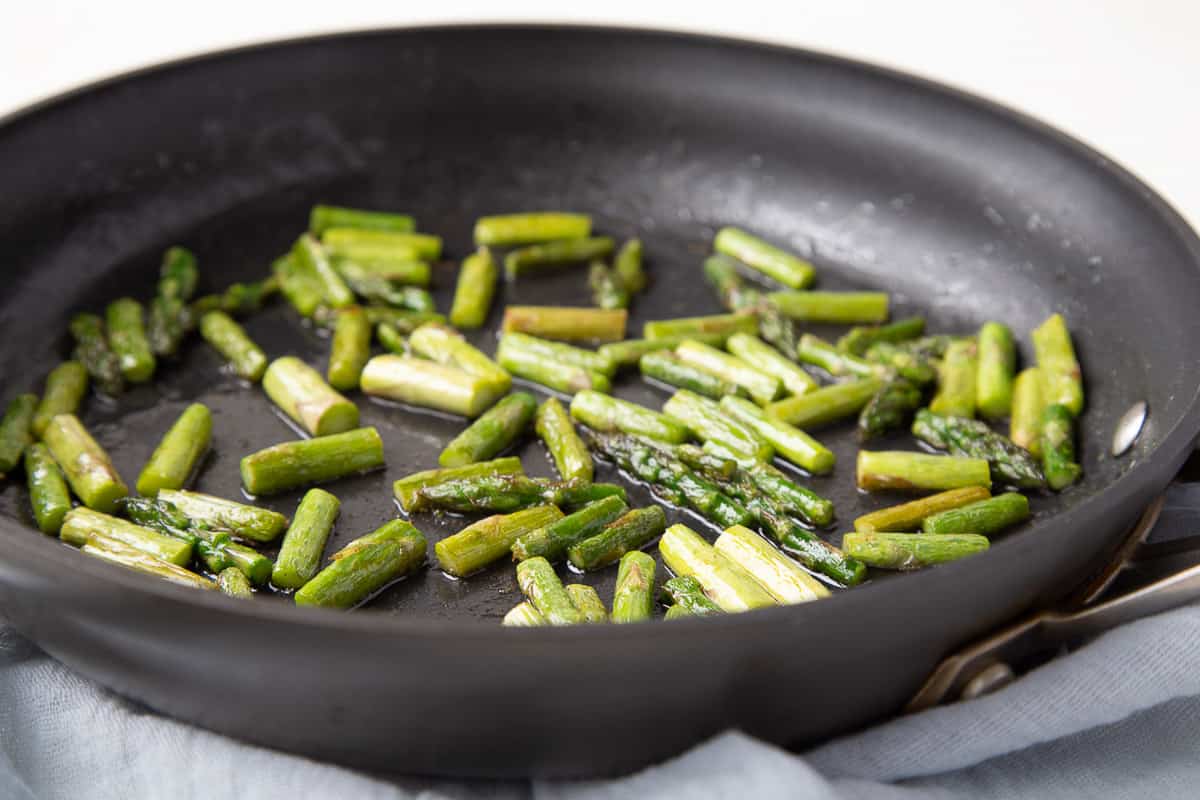 chopped asparagus cooking in a black skillet.