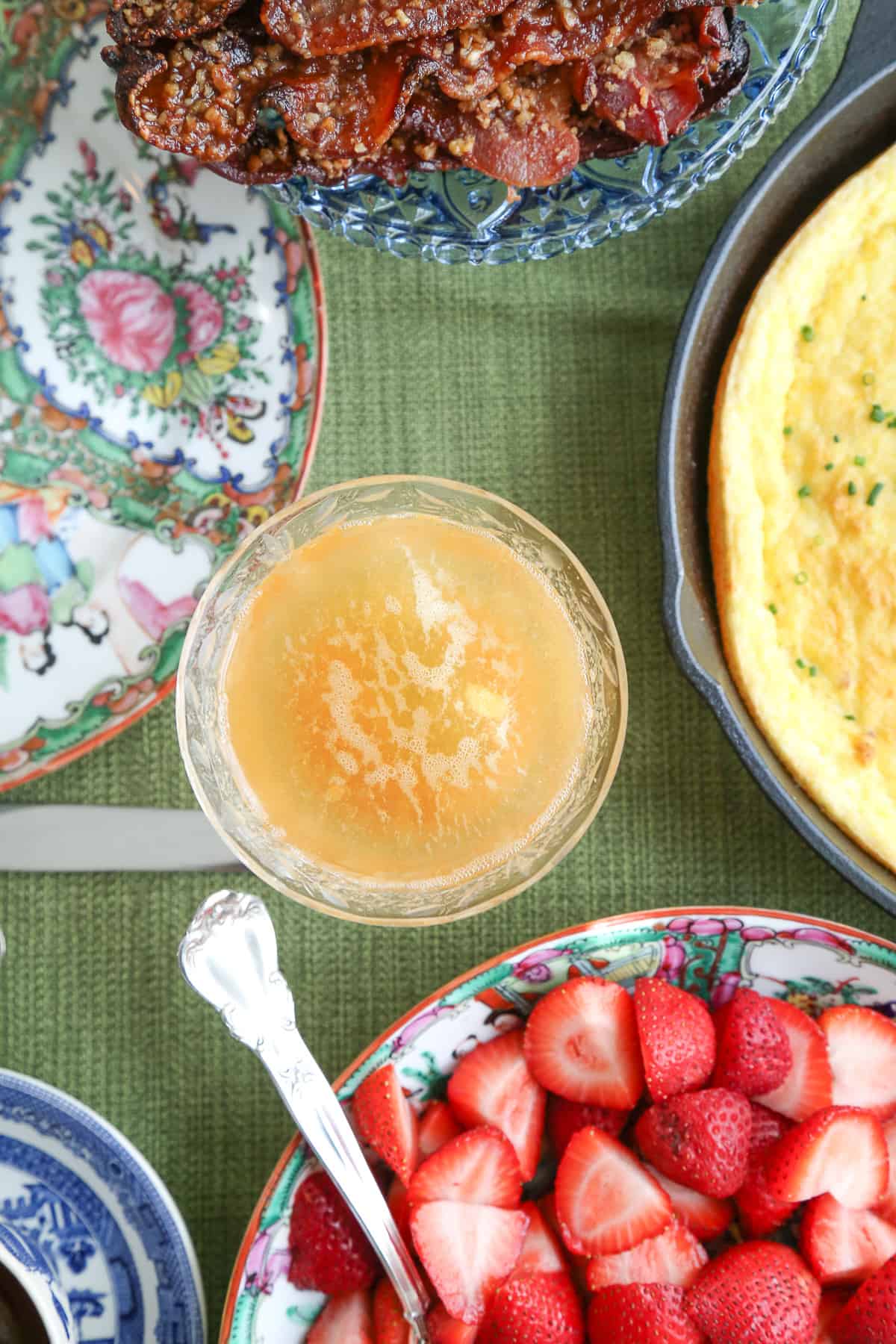 peach apricot bellini in a coupe glass surrounded by berries and bacon.